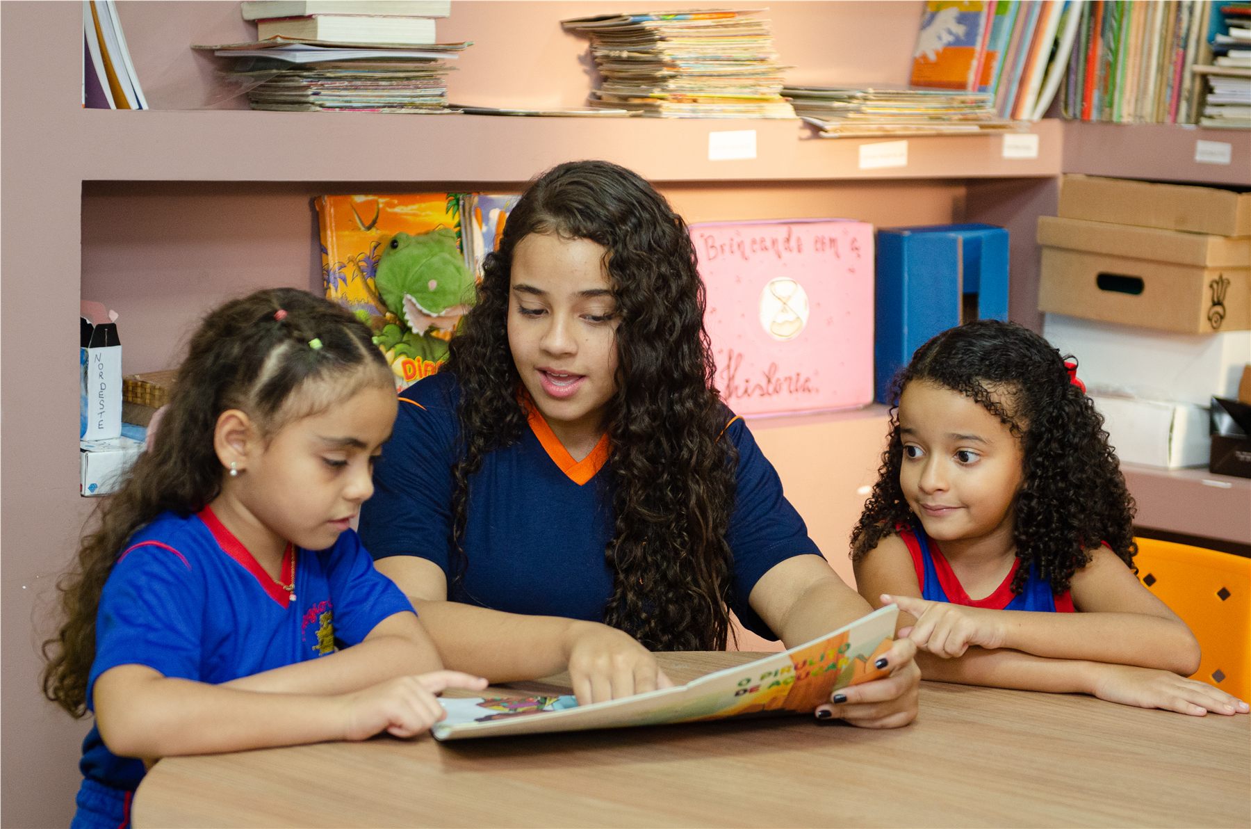 Três estudantes lendo juntas em um espaço da escola